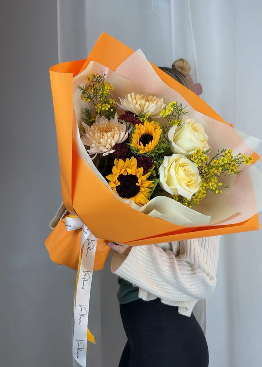 Bouquet of flowers wrapped in orange paper held by a person against a plain background