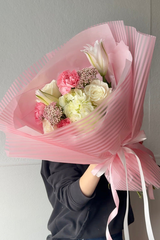 Bouquet of flowers wrapped in pink paper held by a person against a plain background