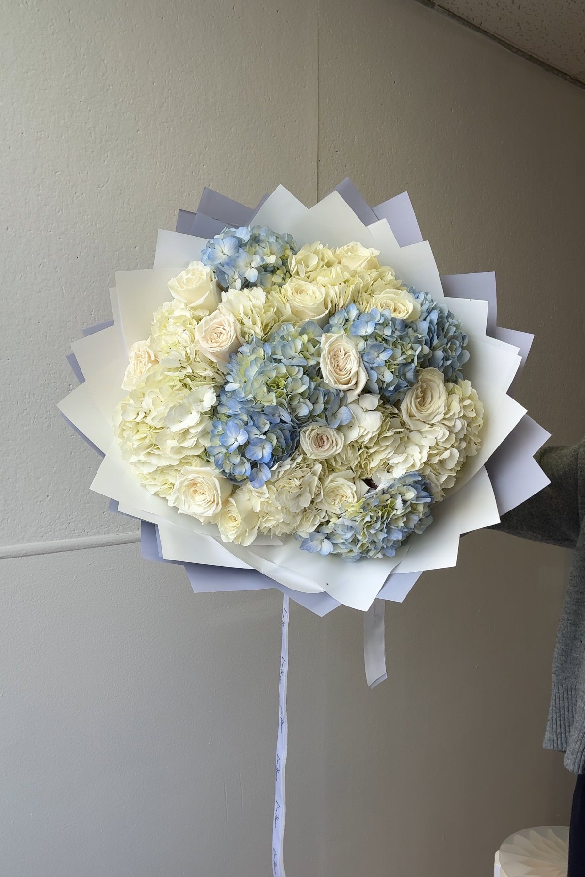 Bouquet of flowers wrapped in white paper against a plain wall.