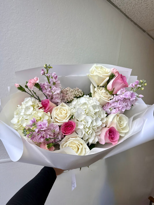 Bouquet of white and pink flowers wrapped in paper against a plain background